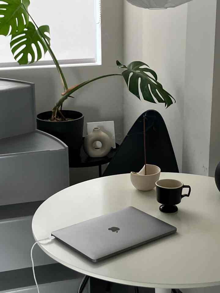 白を基調としたコンパクトな部屋にラウンドテーブル、ノートパソコン、飲み物、植物が配置されたモダンなホームオフィス空間