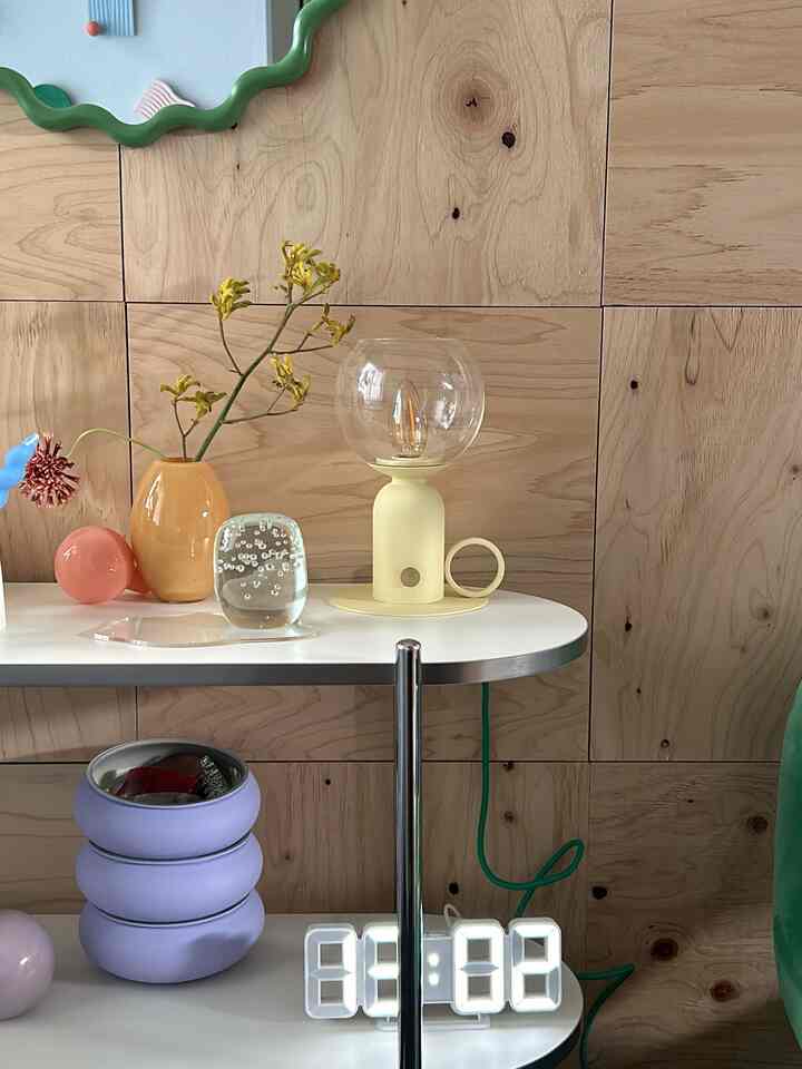 Butter yellow and white toned shelf featuring table lamp, decorative objects, and plants in a charming interior setup