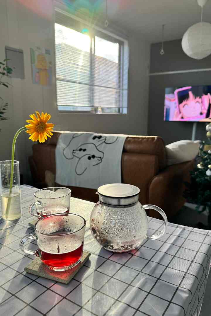 暖かな日差しが差し込むリビング、透明なガラスのティーポットとカップ、ブラウンのレザーソファが配置された雰囲気のあるおうちカフェインテリア