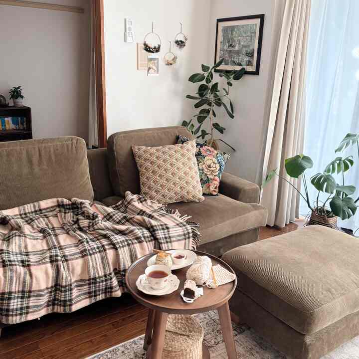 ブラウン系のリビング、コーデュロイソファに花柄クッション、自然な植物が配置された温かみのある印象的な空間