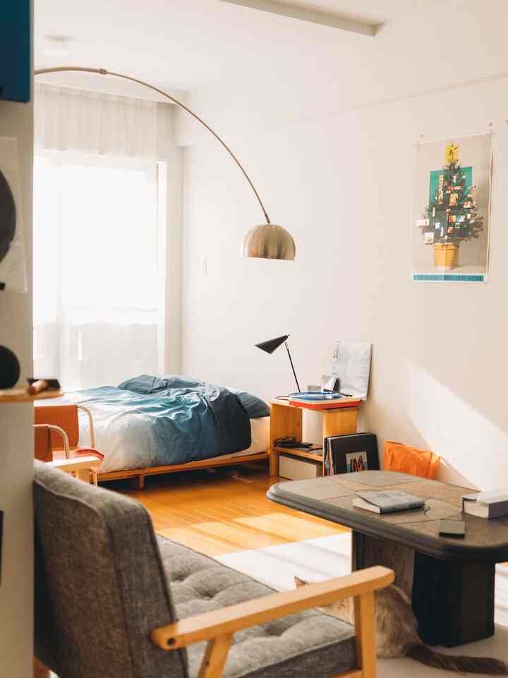 ナチュラルな木目の床と青いベッドカバーがある小さな一人暮らしのリビング兼寝室の空間