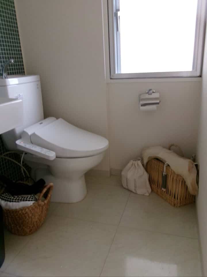 白とナチュラルカラーの調和がある狭いトイレ、コーナーにバスケット収納と窓が配置された清潔感のある空間