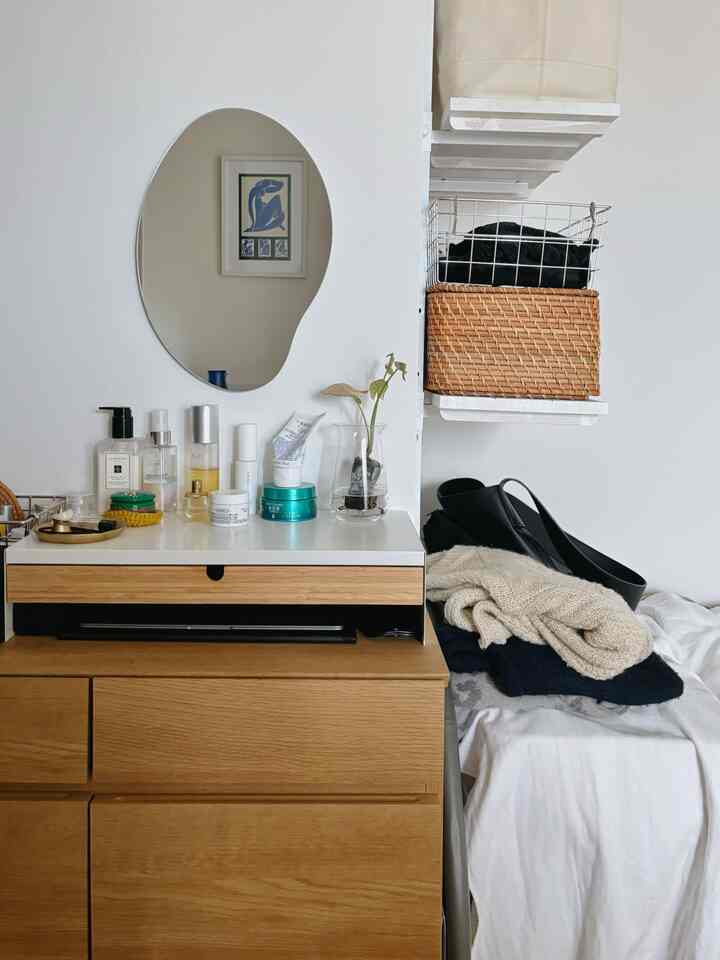 Natural-toned single household bedroom vanity with white walls and wood tone dresser, featuring organized cosmetics and minimal decor