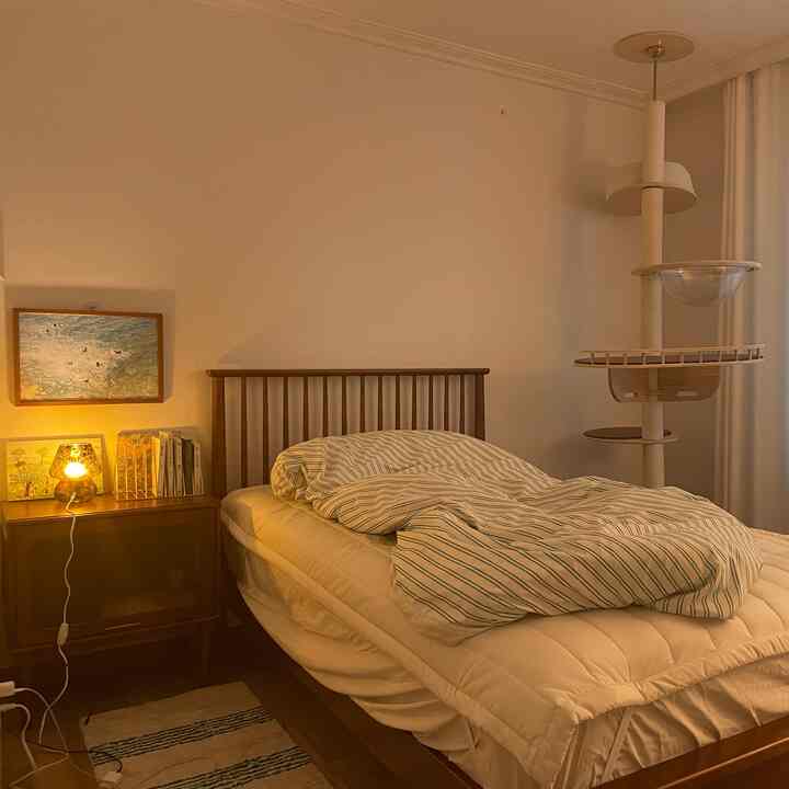 ナチュラルカラーの寝室、木製のベッドフレームとストライプ柄の掛け布団カバーが配置された温かみのあるインテリア