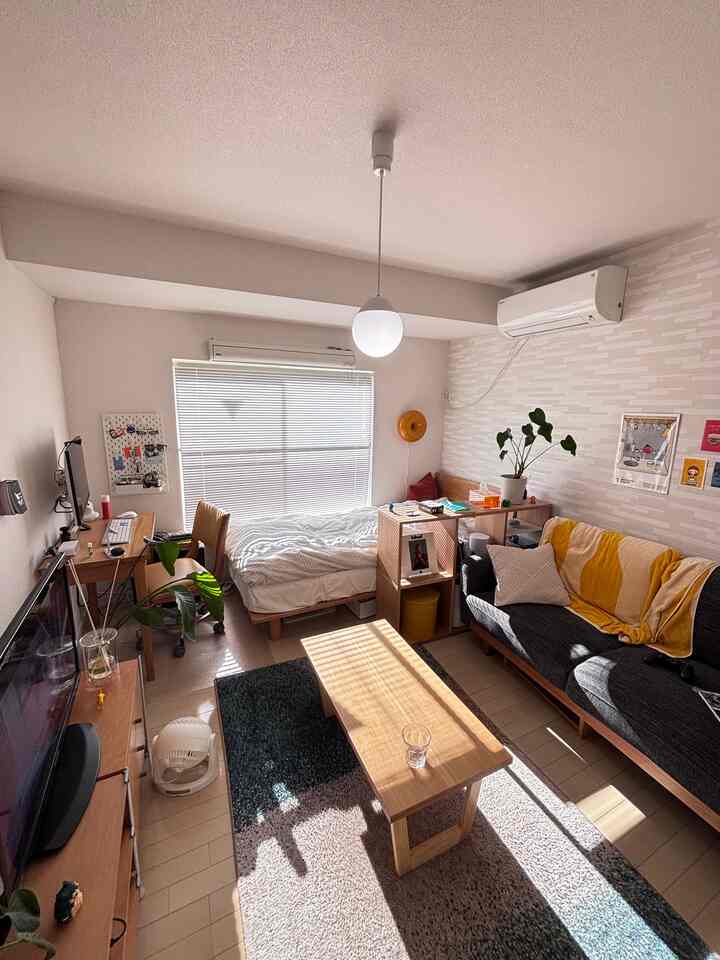 白い壁と木目調家具が調和した7畳の1Kワンルーム、ナチュラルスタイルのソファとベッドが配置された雰囲気のあるインテリア