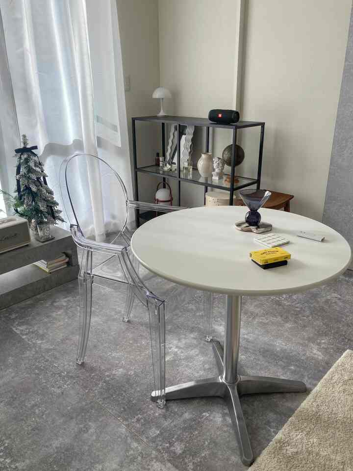 白とグレーのトーンの一人暮らし用リビング、透明なアームチェアと丸テーブルが配置されたシンプルでモノトーンな雰囲気のあるインテリア