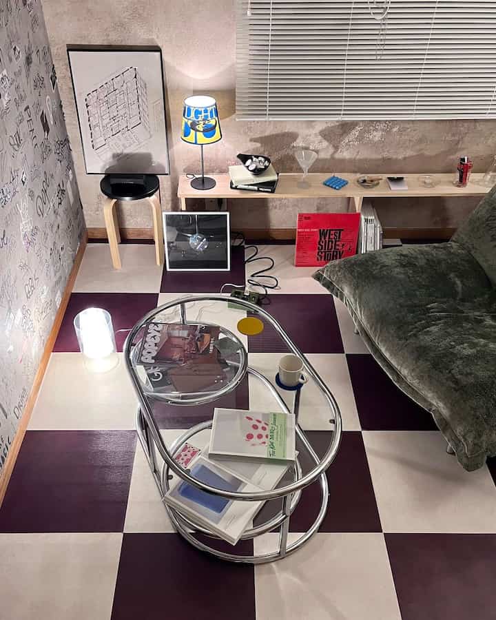 White and purple checkerboard floor vintage-modern living room featuring glass coffee table and green sofa with cozy ambiance