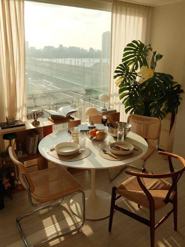 温かみのあるナチュラルな木目調と白を基調としたダイニング、木製の椅子と大きな植物が配置された雰囲気のあるインテリア