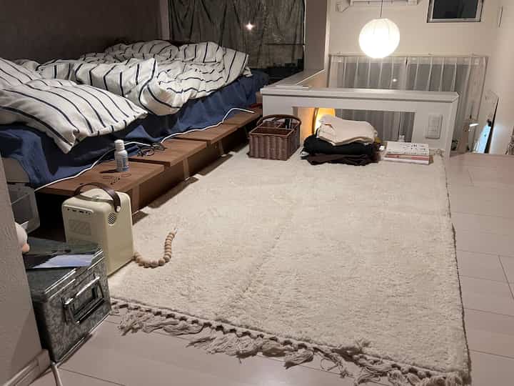 アイボリーとネイビートーンのロフト付きワンルーム寝室、整った寝具とラグが配置された落ち着いた空間