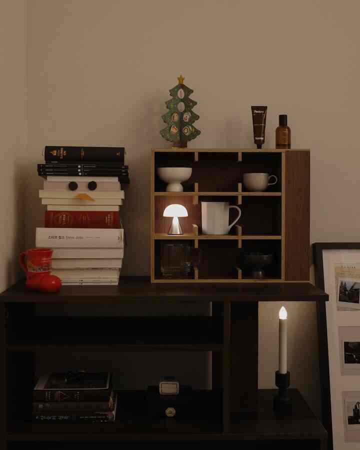 暖かい木目調の書斎、クリスマス装飾とLEDランプ、本とカップ棚が配置された雰囲気のあるインテリア