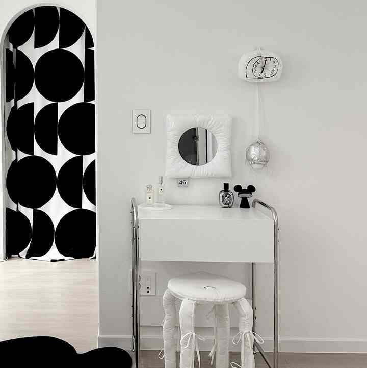 白と黒のトーンのミニマルなリビング、白い化粧台とクッションスツール、大きな丸柄カーテンが調和した印象的な空間