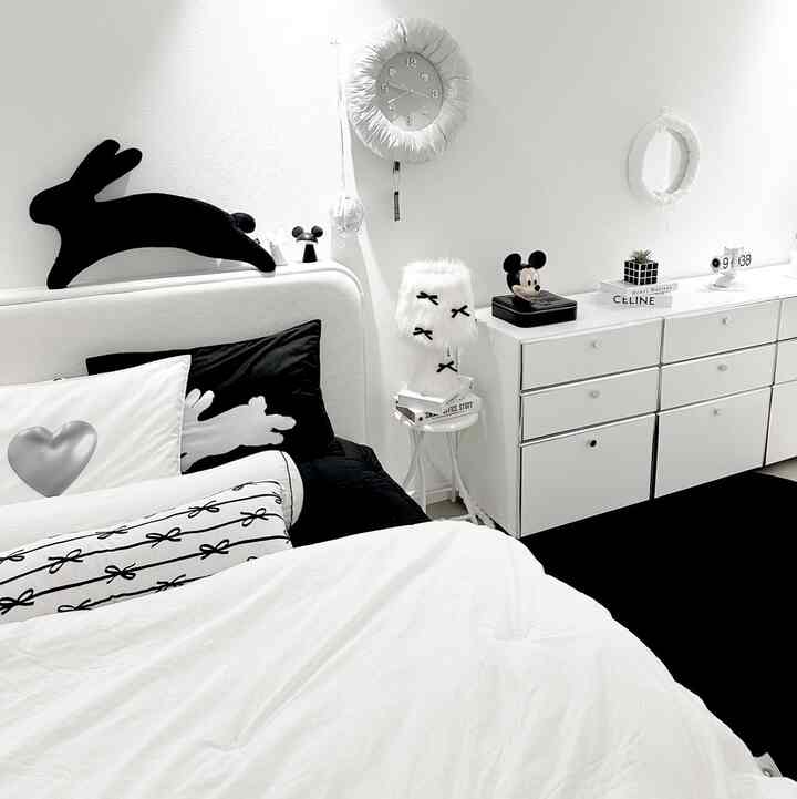 白と黒のトーンが調和した寝室、ベッドとドレッサー、個性的なオブジェと時計が配置された印象的な空間