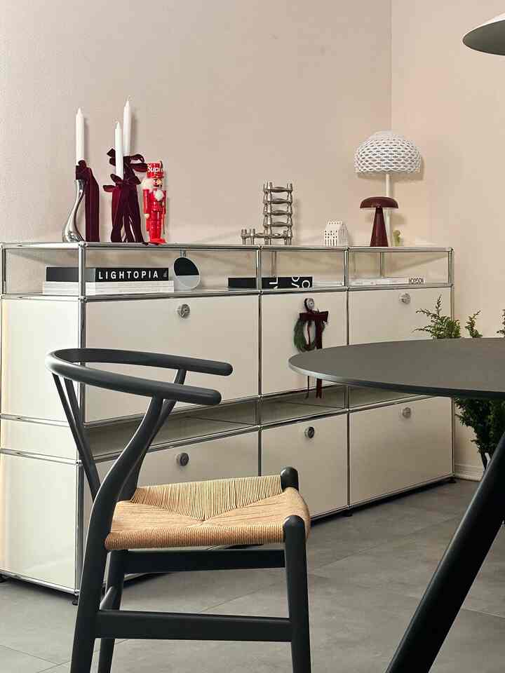 白い壁とモダンなUSMハラー収納キャビネット、黒いCH24チェアと丸いダイニングテーブルが配置されたミニマルなダイニング空間