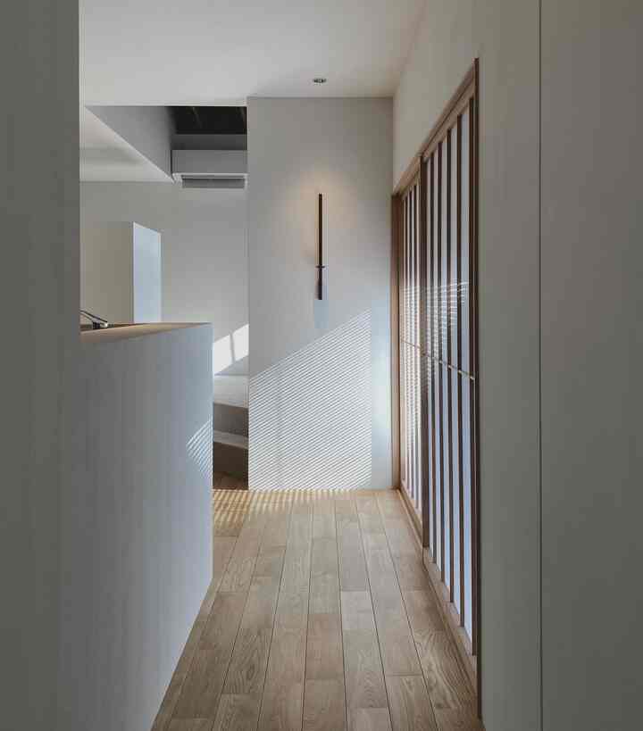 ホワイトと木目調が調和した狭い廊下の空間、ブラインドの影が美しく印象的なミニマルで和モダンなインテリア