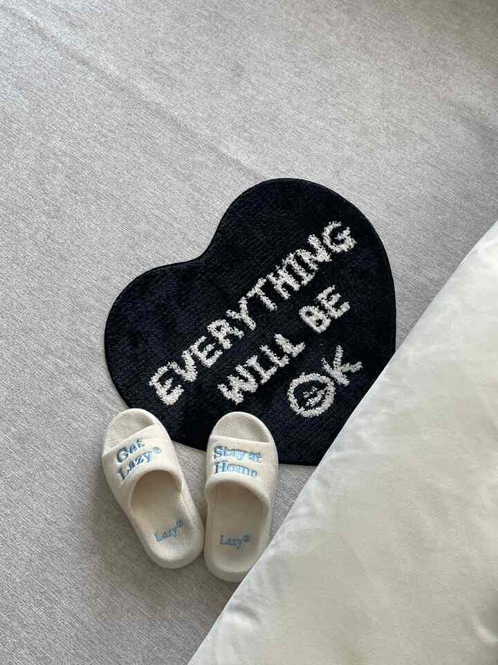 ベージュのトーンの寝室の床に、ハート型の黒いラグと柔らかい白いスリッパが置かれた雰囲気のある空間