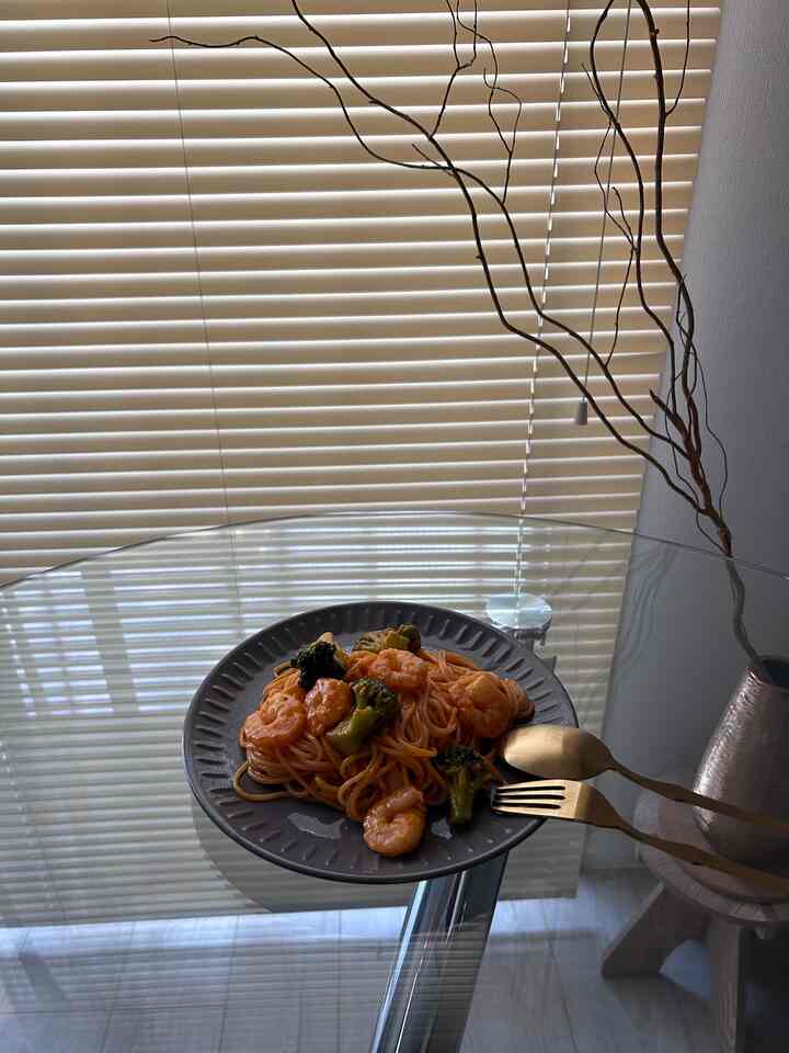 ベージュの色調のリビング、透明なガラステーブルの上にパスタ皿とゴールドのカトラリーが置かれた自然な雰囲気のインテリア