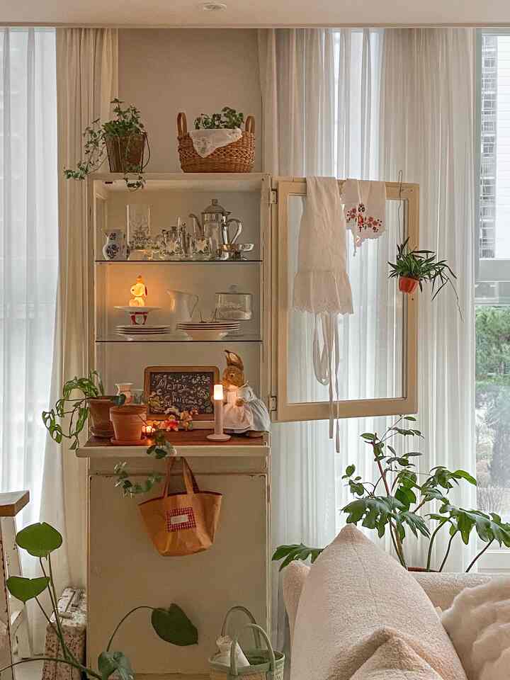 柔らかなアイボリートーンのリビングとキッチンキャビネット、ヴィンテージの小物や植物が調和した雰囲気のあるインテリア