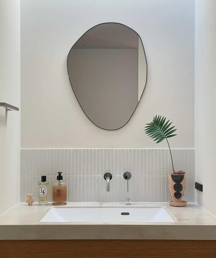 Natural-toned bathroom washbasin space featuring an irregular mirror and potted plant with clean decor