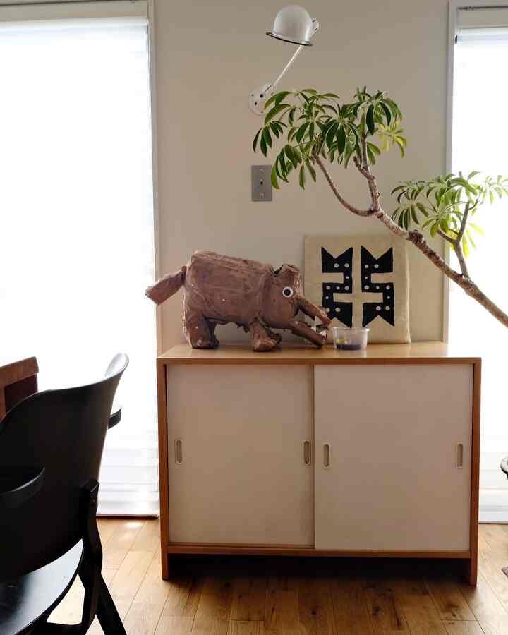 白と木目調の調和するリビング、キャビネットの上にオブジェと大きな観葉植物が配置された雰囲気のある空間