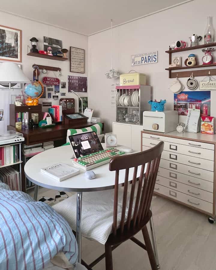 白を基調としたコンパクトなホームオフィス、丸テーブルと木製の椅子、壁の棚とチェストが配置された落ち着いた作業空間