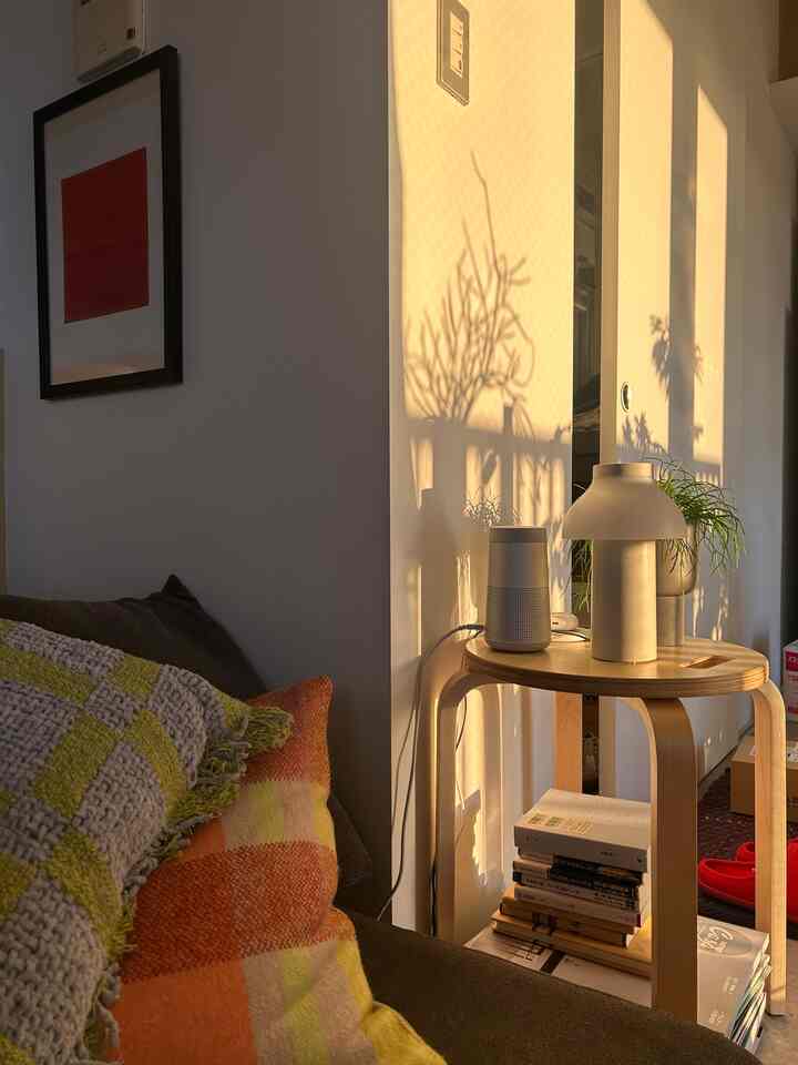 暖かな自然光が差し込むワンルームのリビング、ベージュの木製サイドテーブルとオレンジのクッションが置かれたシンプルなソファ空間