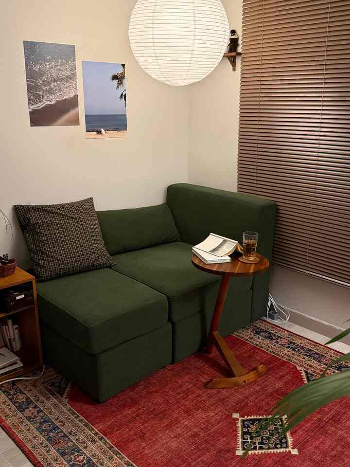 グリーンのソファと赤いエスニックなラグが配置された、ウッド調のブラインドとミニマルな雰囲気のある居心地の良いリビング