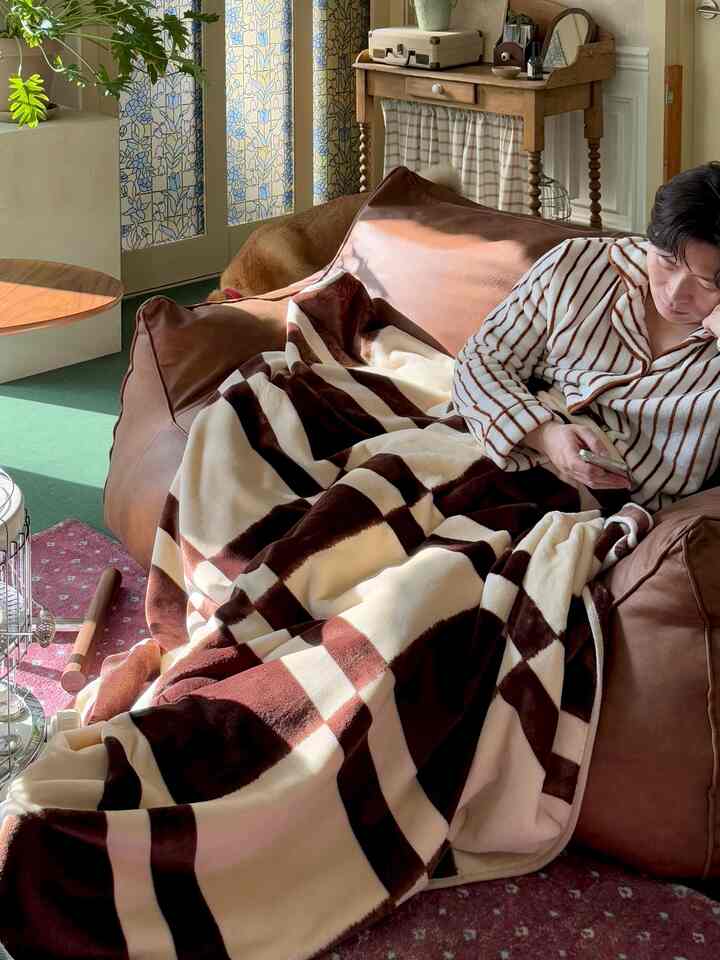 暖かいブラウンとアイボリーのトーンが映えるリビング、ブラウンレザーのビーズクッションとチェック柄のブランケットが居心地の良いナチュラルな空間を演出