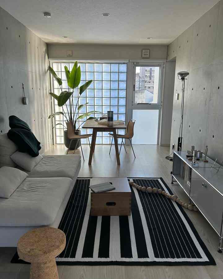 白と黒のトーンのリビング兼ダイニングルーム、白のセクショナルソファと木製のダイニングテーブル、大きな植物が配置されたモダンな空間