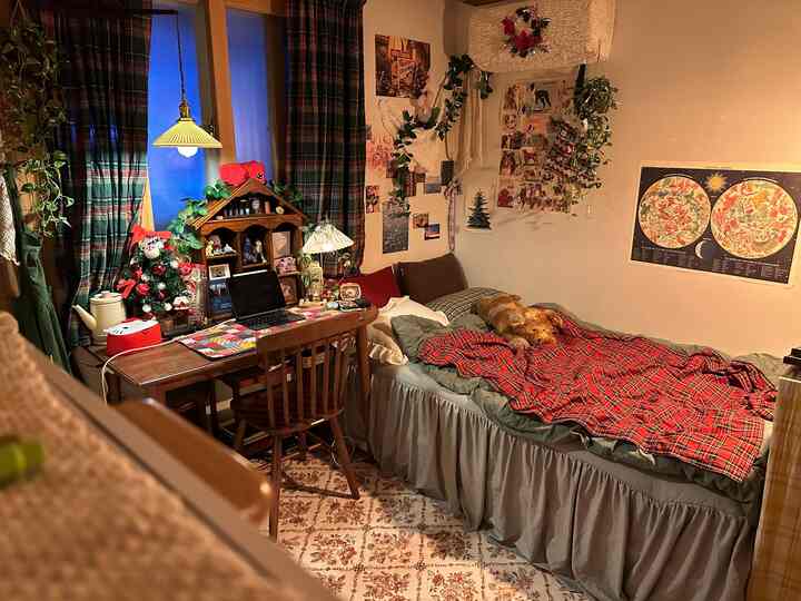 温かみのある木目調とチェック柄のカーテンがあるワンルーム、デスクとベッドが配置された雰囲気のあるヴィンテージ空間