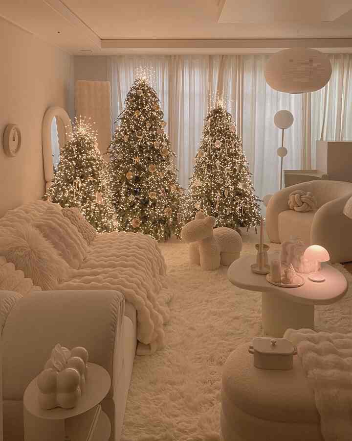 アイボリー調のリビングルーム、中央背景に三つのクリスマスツリーが輝き、ファーブランケットとソファ、ラグで温かみのある雰囲気を演出した空間