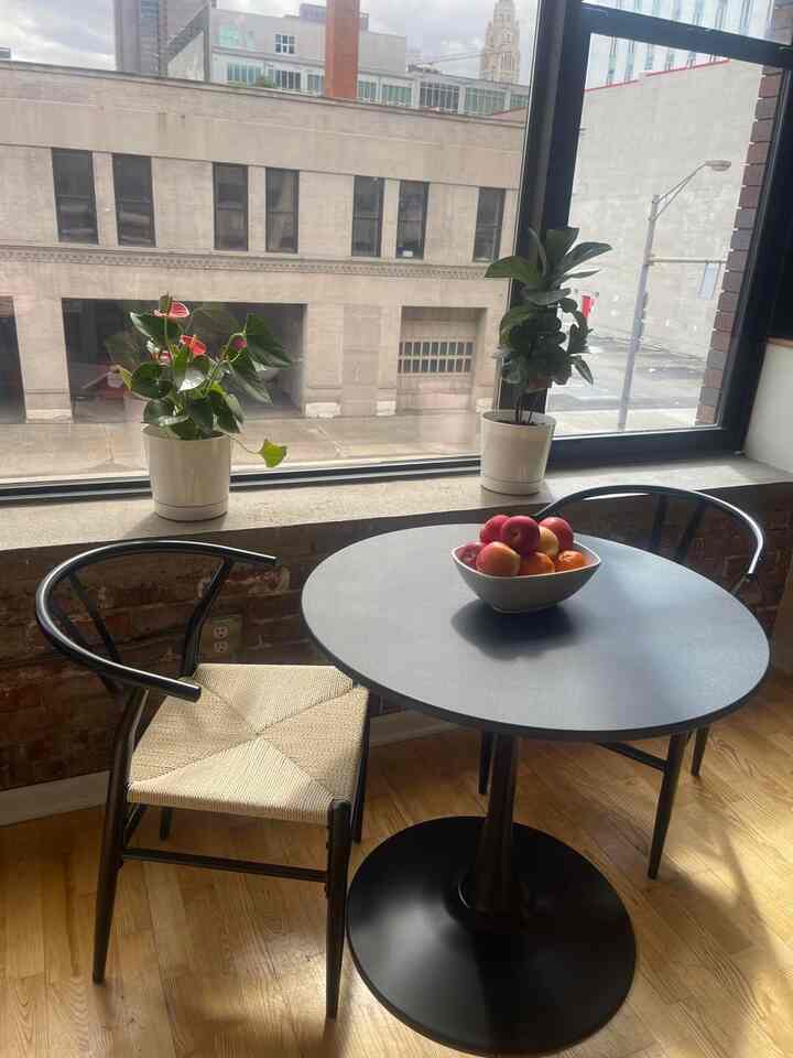 Modern black coffee table with deep wooden floor, plants on the windowsill, and a bowl of fruit in a cozy dining space