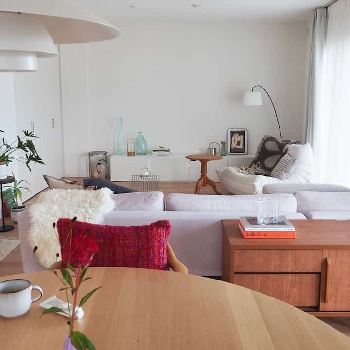 白い壁と木目調の家具が調和するスカンジナビアスタイルのリビング、ルビーレッドのクッションがアクセントの快適な空間