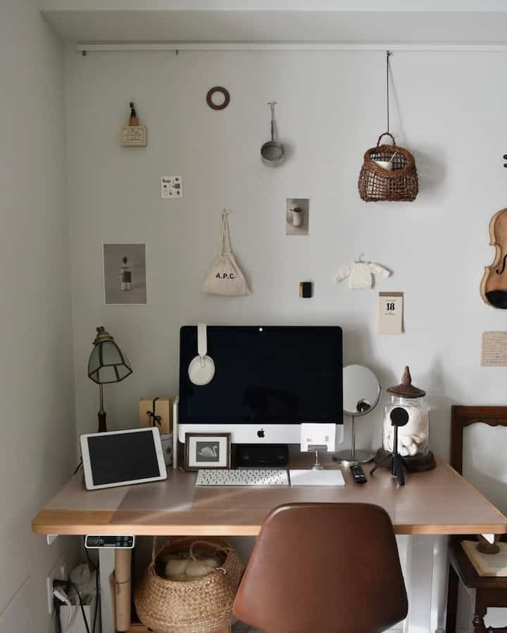 ナチュラルな色調の書斎ワークスペース、木製デスクとブラウンレザーの椅子、ラタンバスケットやヴィンテージの壁掛け飾りが調和する空間