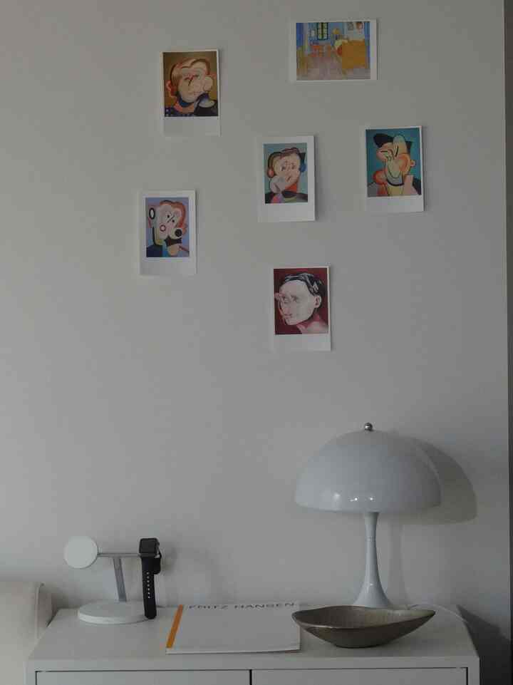 白を基調とした空間、壁には複数の絵が配置されており、サイドテーブルの上にテーブルランプとトレイが置かれた落ち着いたインテリア。