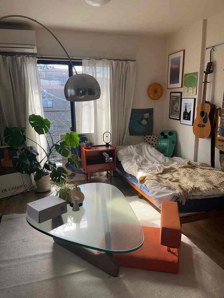 白い壁と緑の植物が調和する8畳のワンルーム、ミッドセンチュリーモダン家具とコーヒーテーブルが配置された印象的な一人暮らしのリビング空間