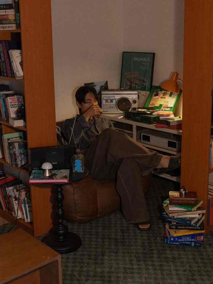 暖かみのあるブラウンとグリーンの色調のリビング、ビーズクッションソファと本棚が配置されたカフェ風の落ち着いたインテリア