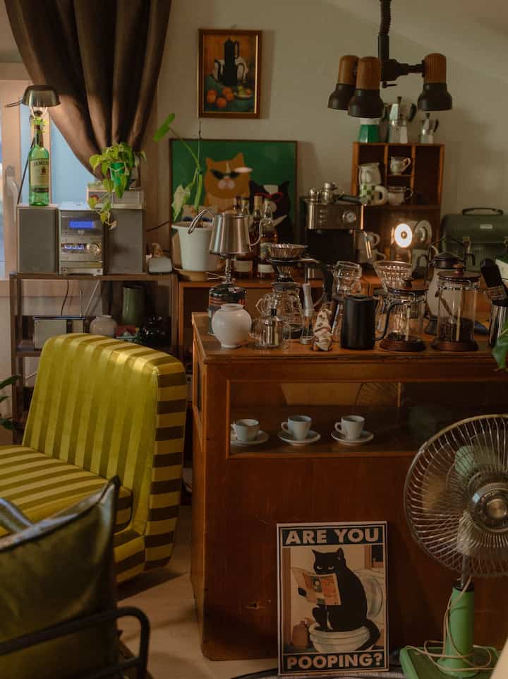温かみのあるブラウンの木目調とグリーンが調和したカフェ風リビング、コーヒー器具と猫のアートが配置された雰囲気あるインテリア