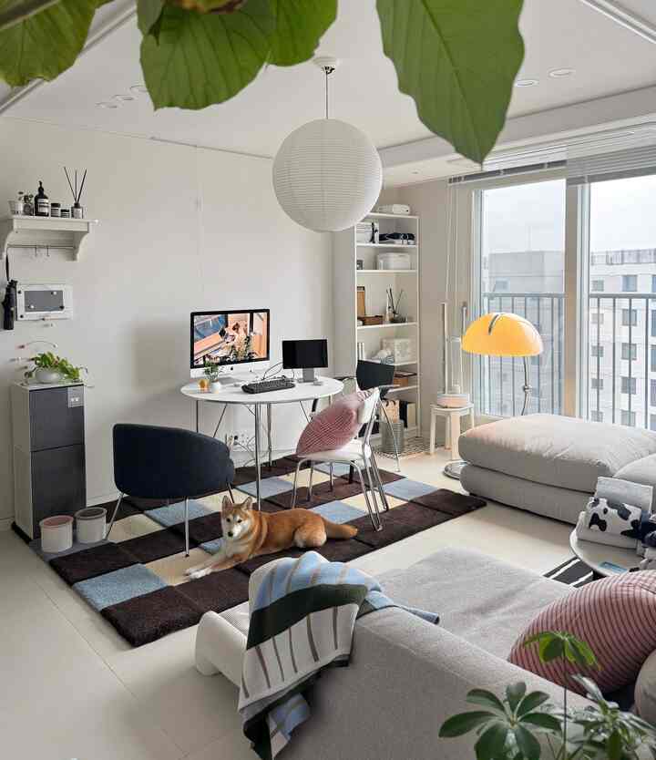 白と茶色のトーンのリビング、広いソファと丸テーブルが配置され、チェック柄のラグの上で犬がくつろぐ雰囲気のあるインテリア