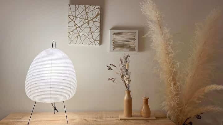 ナチュラルカラーと木目調が調和した寝室の小さなテーブルにイサム・ノグチのAKARIスタンドランプと花瓶が置かれた雰囲気のあるインテリア