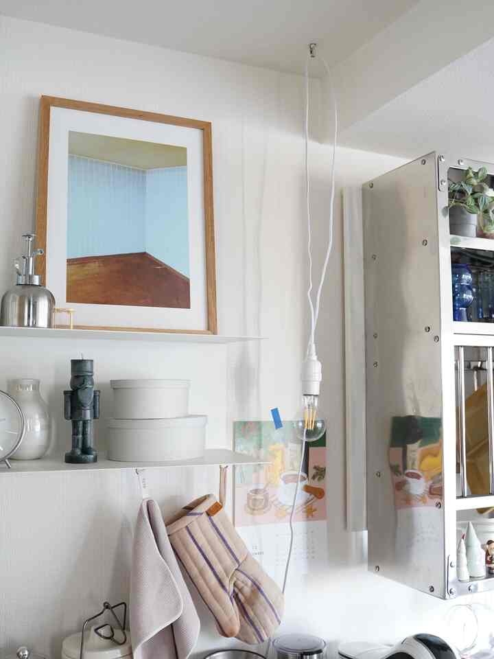 Bright white kitchen space with natural wood tones, featuring a framed poster, hanging light bulb, and organized kitchen accessories