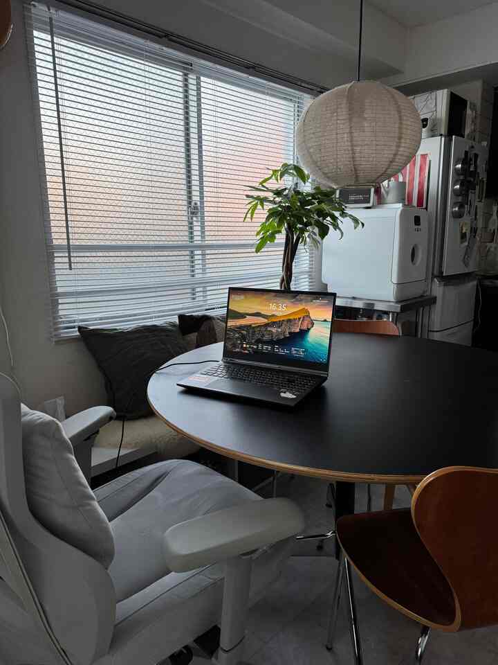 明るい白と茶色の色調のキッチン兼ホームオフィス空間、丸テーブルとノートパソコン、椅子が配置された実用的なインテリア