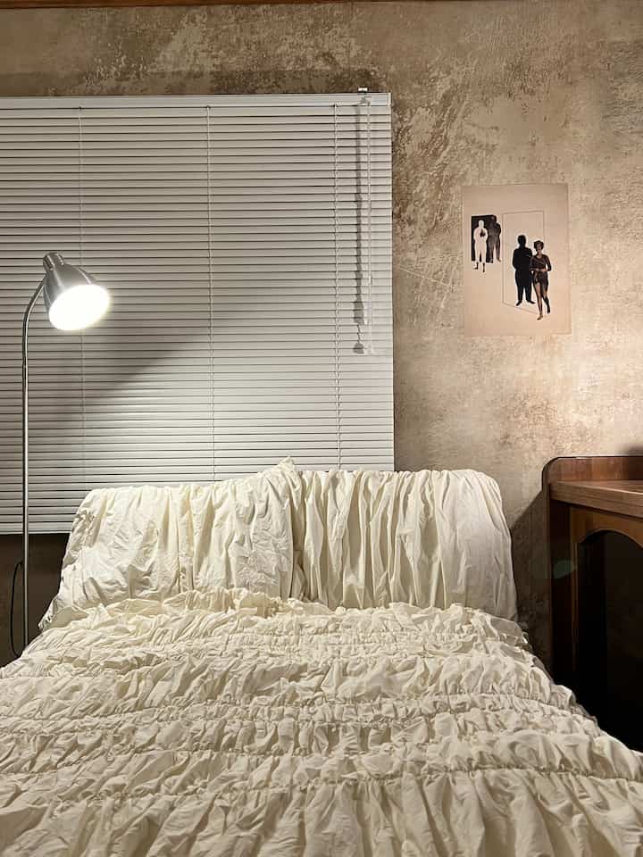 アイボリーとグレーのトーンの寝室、フリルの寝具とコンクリート調の壁が配置された雰囲気あるインテリア