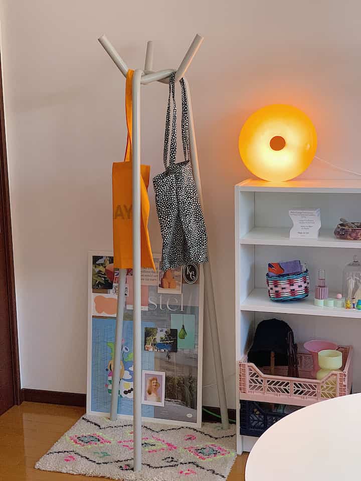 白と茶色のトーンの1LDK空間、中央にシンプルなコートハンガーと照明と小物のある棚が配置された雰囲気のあるインテリア