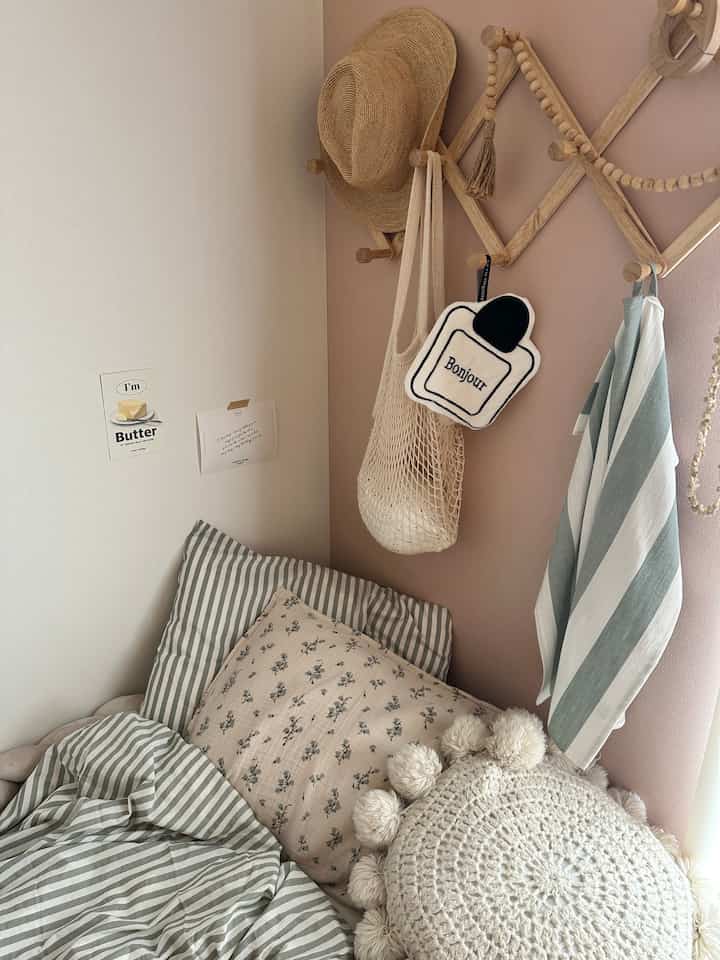 柔らかなピンクの壁とグリーンのストライプ寝具が配置された北欧風の子供部屋の温かみのあるインテリア