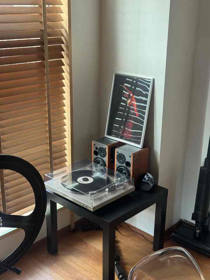 木目調のブラインドと床、黒い四角いテーブルにターンテーブルとスピーカーが置かれたモダンなコーナースペース