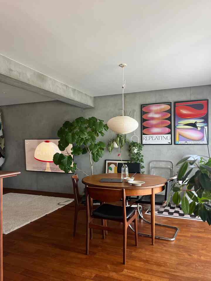 温かみのある木目調とグレーコンクリートが調和したミッドセンチュリーモダンのリビング、円形のダイニングテーブルと植物、ポスターが配置された印象的な空間