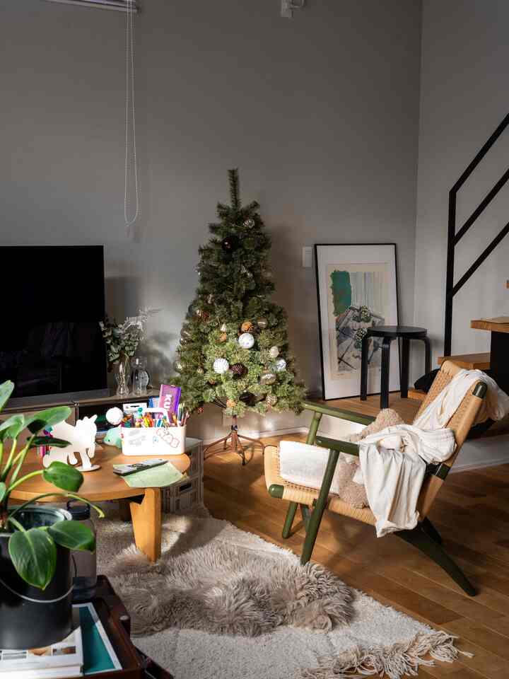 ナチュラルトーンのリビング、中央に飾られたクリスマスツリーと居心地の良いラグ、子供のおもちゃとアームチェアが配置された雰囲気のある空間