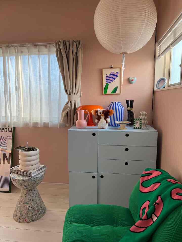 温かみのあるベージュ色の壁と淡い青の収納キャビネットが配置されたコンパクトなリビング、緑のアームチェアと多彩な装飾品が置かれた雰囲気のあるインテリア