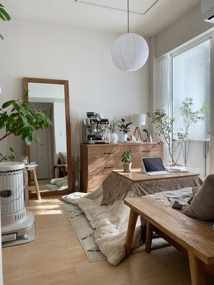 白い背景と木目調の家具が調和した北欧風リビング、こたつと植物が配置され、落ち着いた雰囲気のあるインテリア