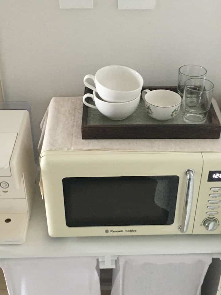 白を基調としたキッチン、レトロな電子レンジとコーヒーカップやグラスのトレイが配置された雰囲気のある空間